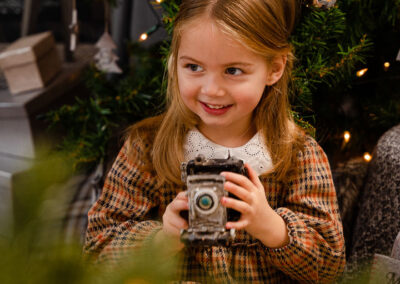 Ein Mädchen mit schönem Kleid sitzt vor einem Weihnachtsbaum und hat eine alte Kamera in der Hand