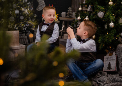 Ein Junge im Anzug fotografiert seinen Bruder mit einer alten Kamera. Beide sitzen in einem weihnachtlich geschmückten Wohnzimmer