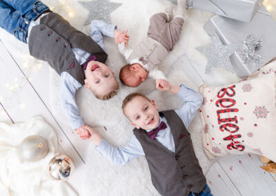 Drei Jungs mit schicken Anzügen liegen sternenförmig auf dem Boden und lachen und halt sich an den Händen. Perfektes Geschenk zu Weihnachten