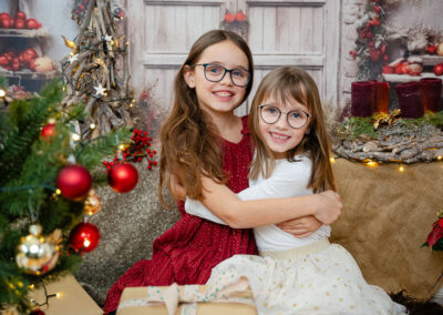 Zwei Mädchen mit Brillen. Ein Mädchen hat ein rotes Kleid das andere ein weisses Kleid. Weihnachtliches Foto mit festlich geschmückter Tür