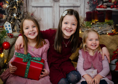 Drei Mädchen lachen in die Kamera. Ein Kind hat ein geschenk in der Hand auf dem Schoss