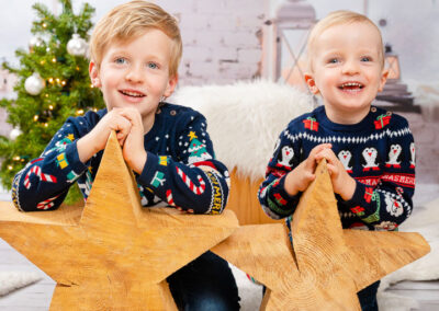 Zwei lachende Kinder bei einem Weihnachtsfotoshooting. Sie lehnen sich auf zwei Holzsterne
