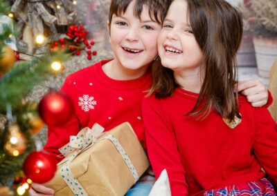 Geschwisterpärchen mit roten Oberteilen sitzen im weihnachtlichen Hintergrund