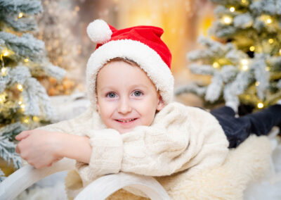 Ein Junge liegt auf einem Schlitten und hat eine rote Zipfelmütze auf