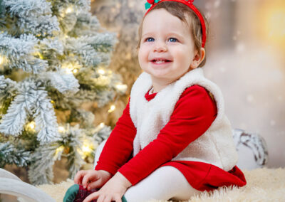 Ein kleines Mädchen sitzt auf einem Schlitten und hat eine Rentier-Haarspange auf dem Kopf