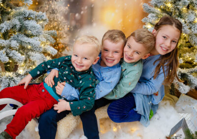 Vier Kinder sitzen bei einem Fotoshooting auf einem Schlitten und lachen