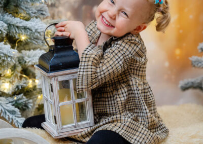 Ein blondes Mädchen sitzt auf einem Schlitten mit einer Laterne und lacht